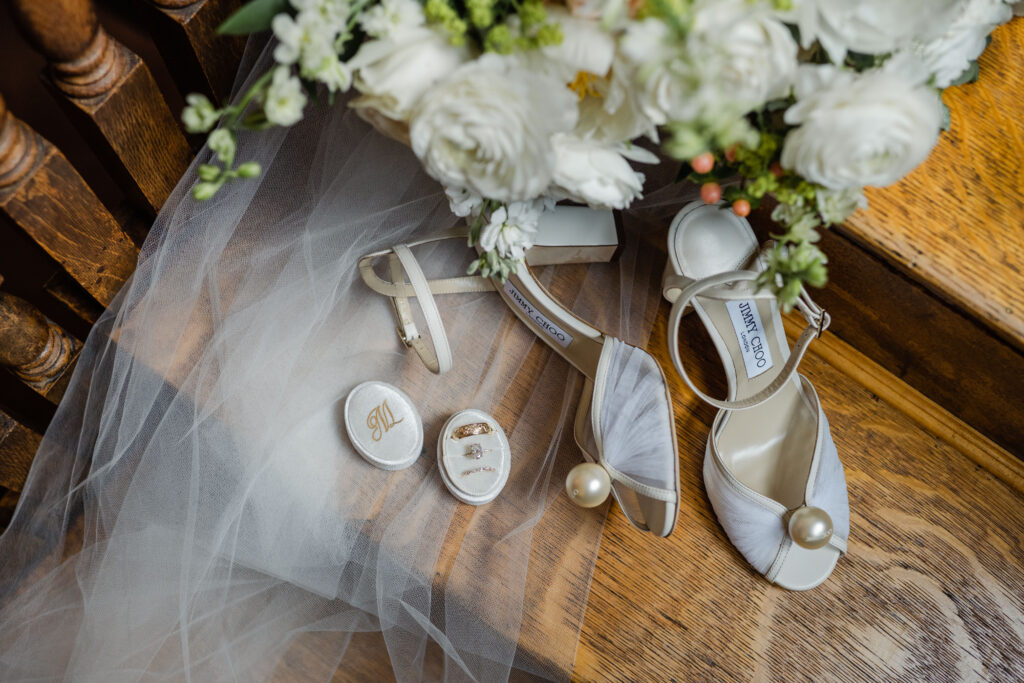 A close-up shot of wedding rings, bouquet and shoes on a veil cascading down wooden stairs.